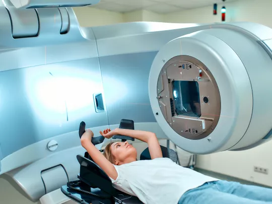 放射線治療装置の前で医療用カウチに横たわる女性。