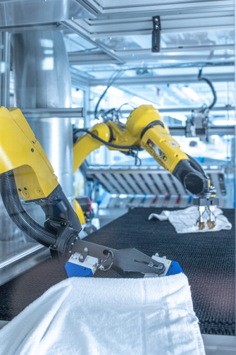 IDSの2Dおよび3Dカメラの助けを借りて、2台のロボットが工業用ランドリーで洗濯物を広げている。