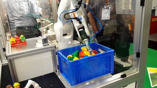 セル内のロボットが、色つきの物体が入った青い箱に手を伸ばす